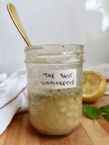 Stirring the vinaigrette in the jar using a golden spoon on a wooden board