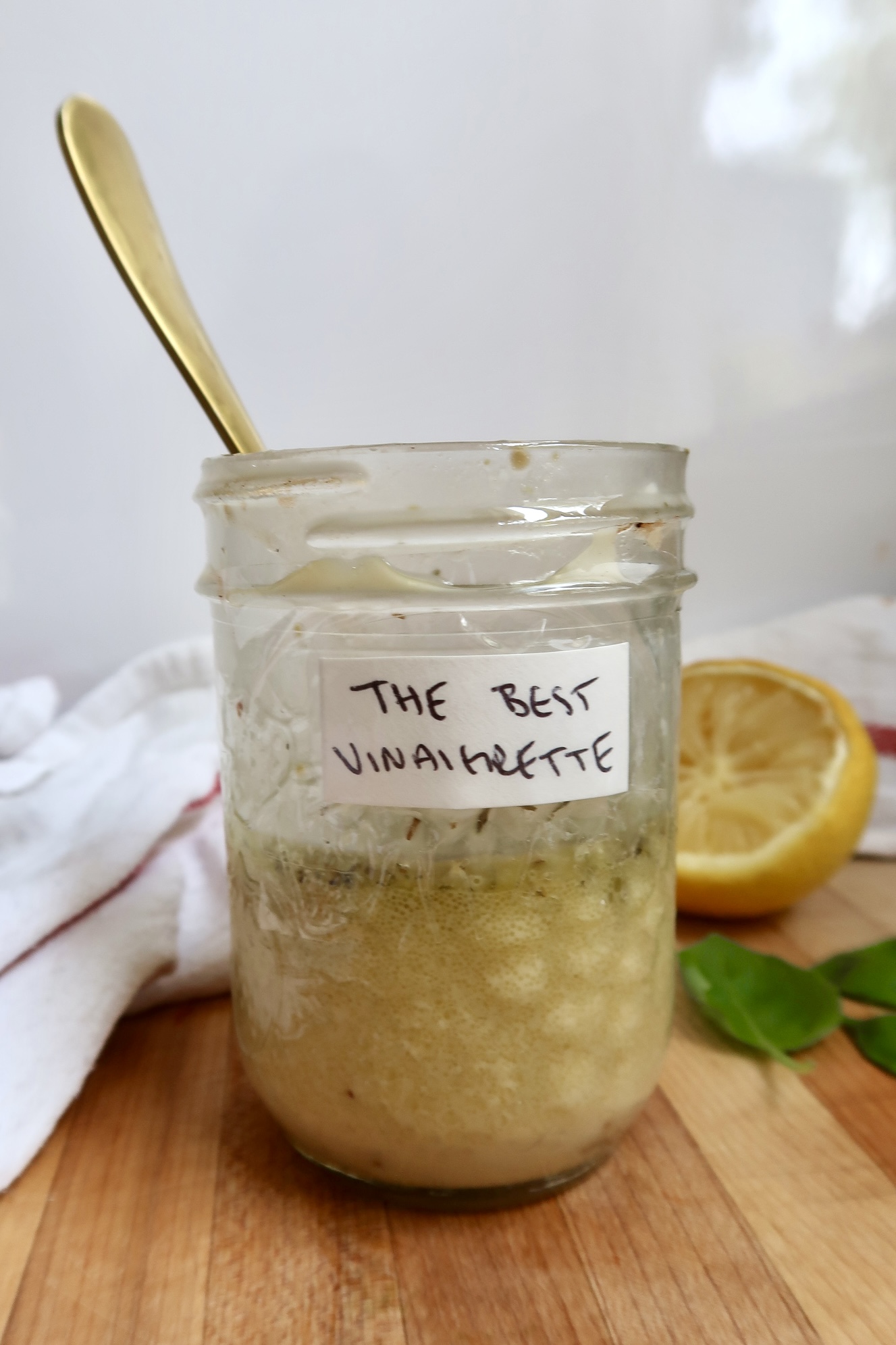 Stirring the vinaigrette in the jar using a golden spoon on a wooden board