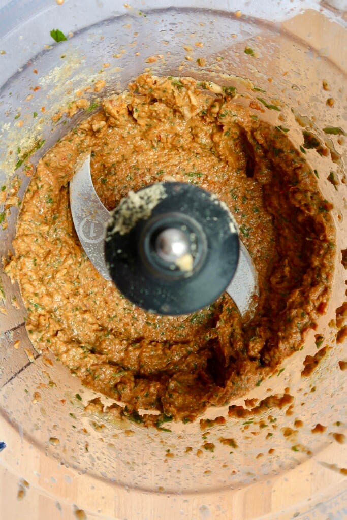Close-up of food processor bowl showing thick, creamy sundried tomato pesto around the blade.