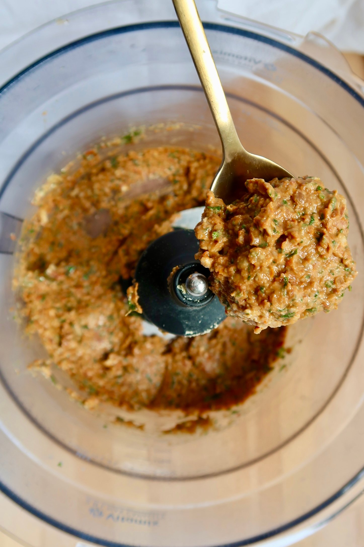 Food processor bowl with freshly blended sundried tomato pesto and a spoon inside.