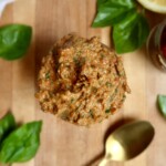 Large spoonful of sundried tomato pesto held over a wooden surface with fresh basil and a gold spoon nearby.