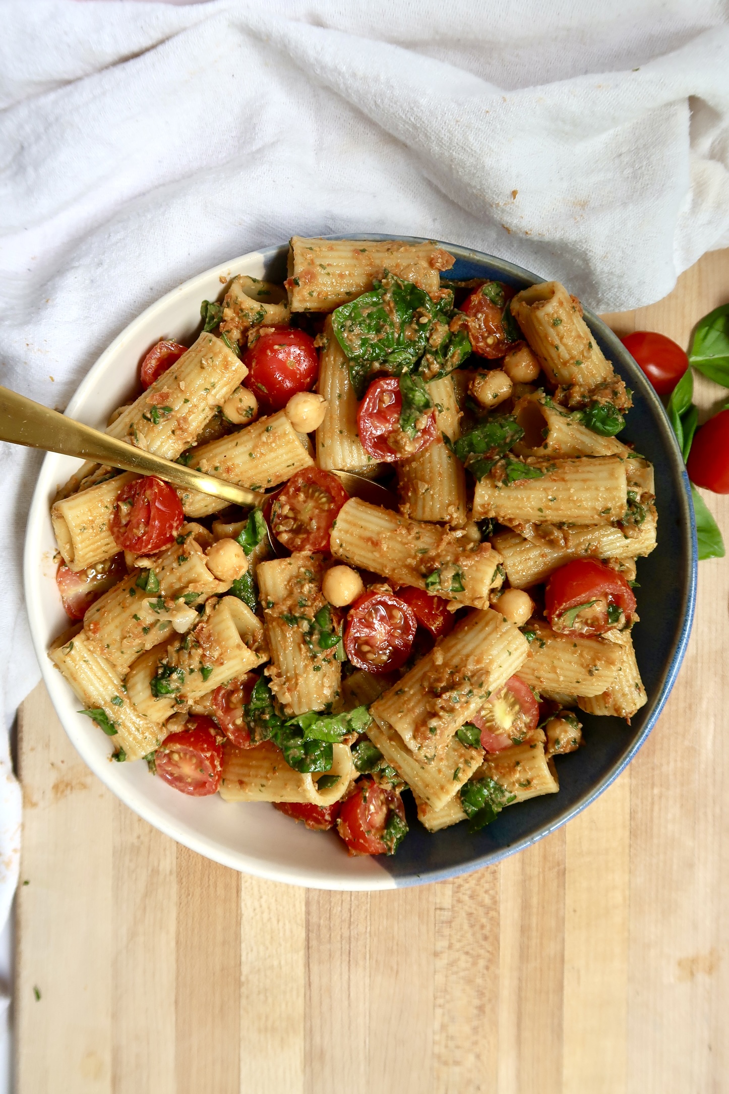Bowl of pasta tossed with cherry tomatoes and a dollop of green pesto, served with a gold fork.