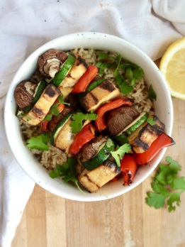 Bowl of grilled tofu skewers with veggies served over rice, garnished with fresh cilantro and a lemon wedge.