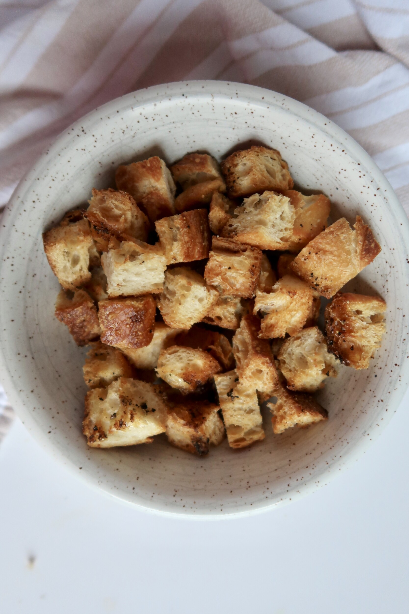 Golden brown croutons in a speckled bowl – Freshly baked and crispy with visible seasoning.