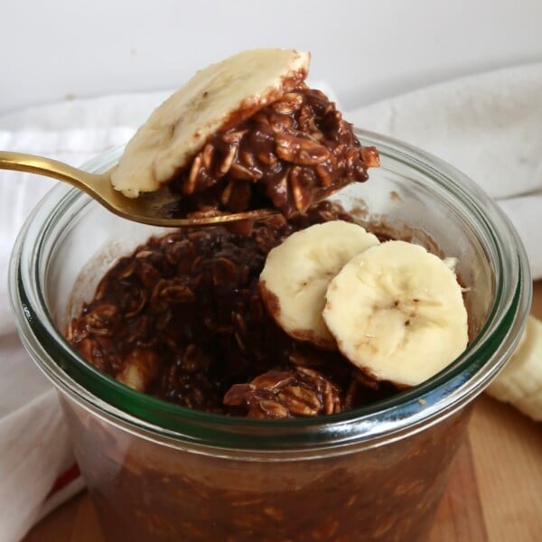 Spoonful of chocolate banana overnight oats lifted from a glass jar, topped with fresh banana slices.