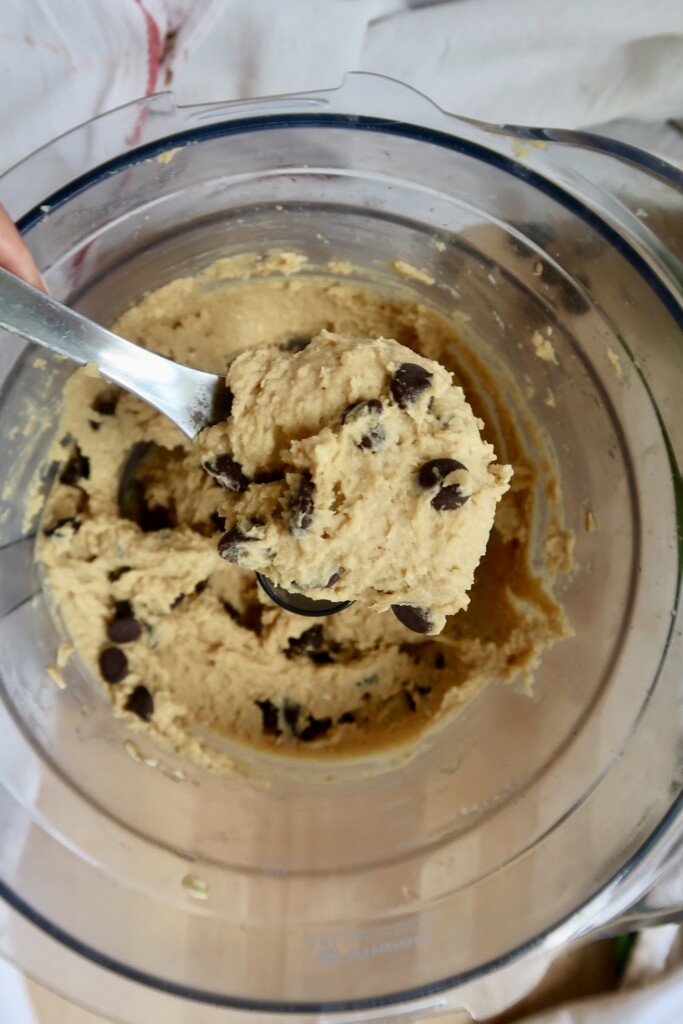 Close-up of chickpea cookie dough with chocolate chips inside a food processor bowl.
