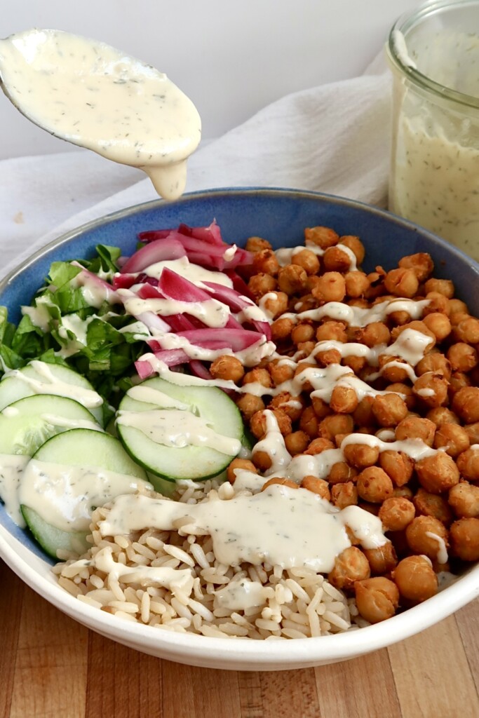 Spoon drizzling dill sauce over buffalo chickpeas, cucumber and brown rice.