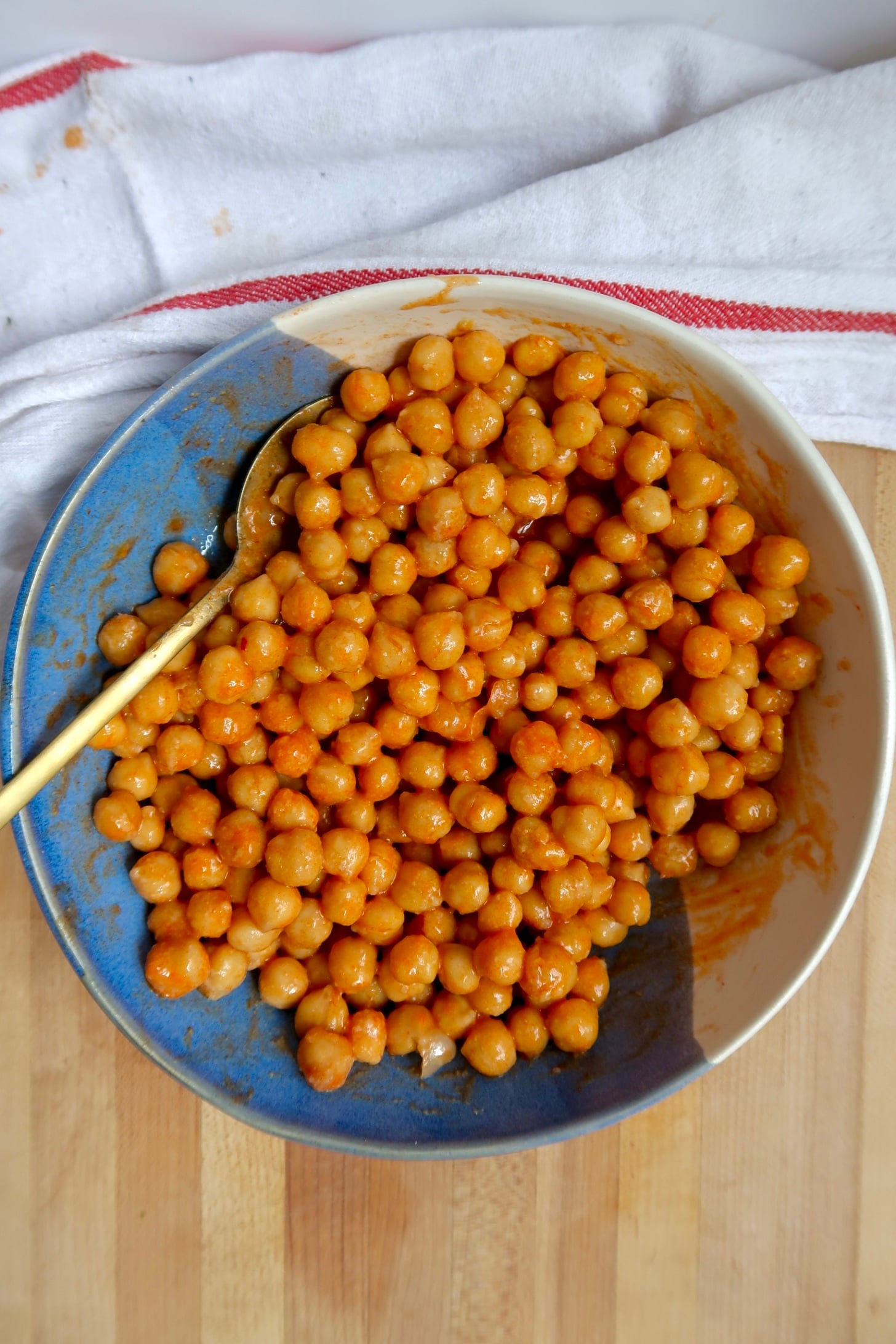 Chickpeas tossed in buffalo sauce mixture in a bowl with a wooden spoon.