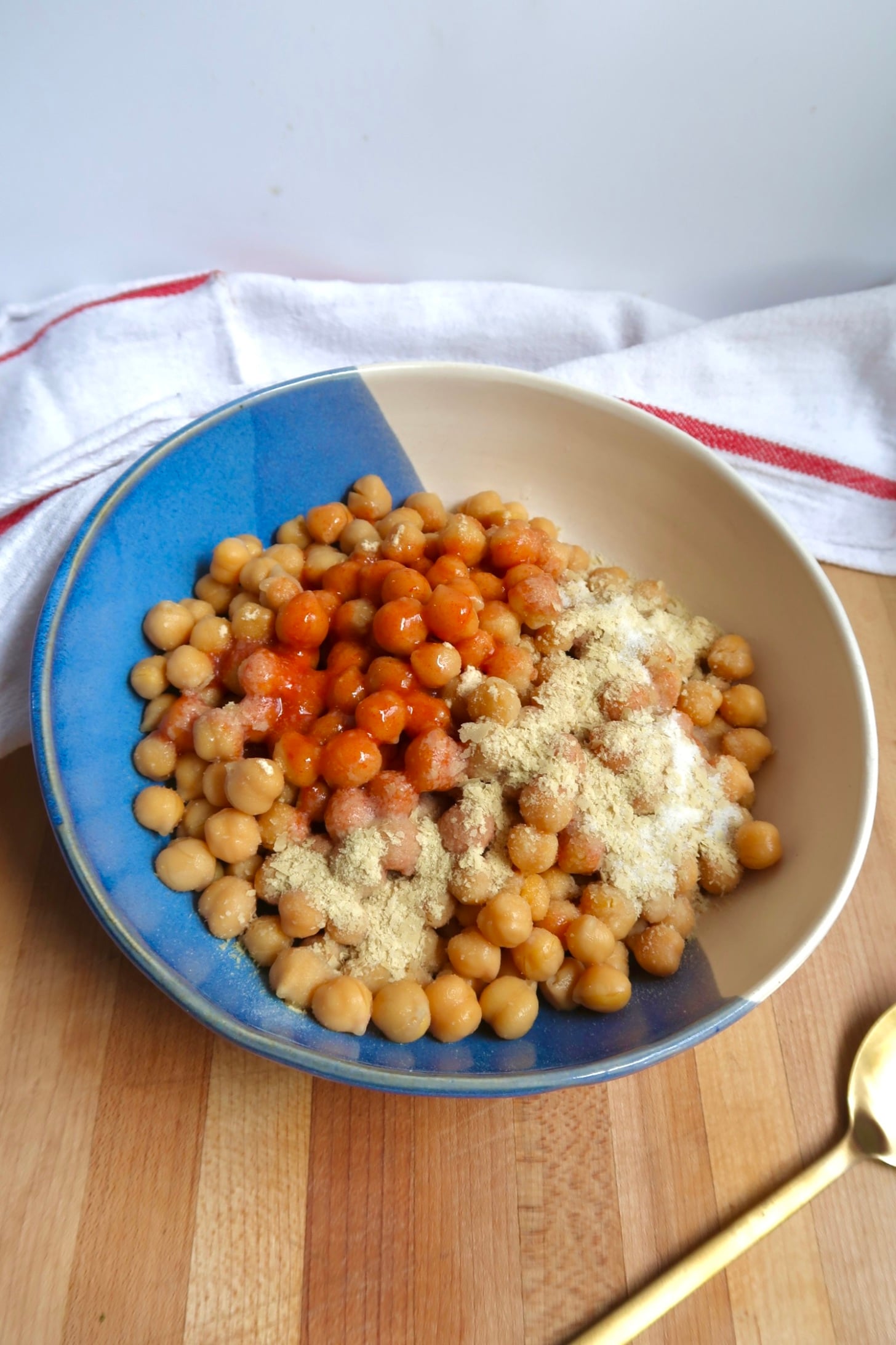 Chickpeas in a mixing bowl with hot sauce, nutritional yeast, and spices.