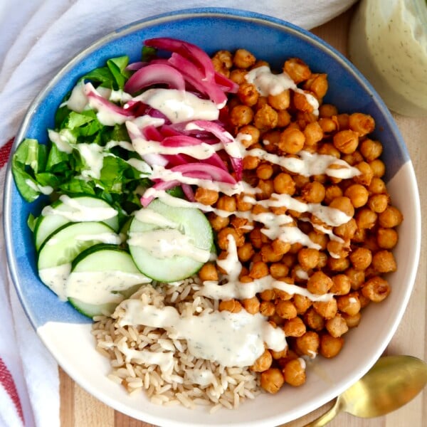 Grain bowl topped with buffalo chickpeas, cucumber, greens, pickled onions, and sauce.