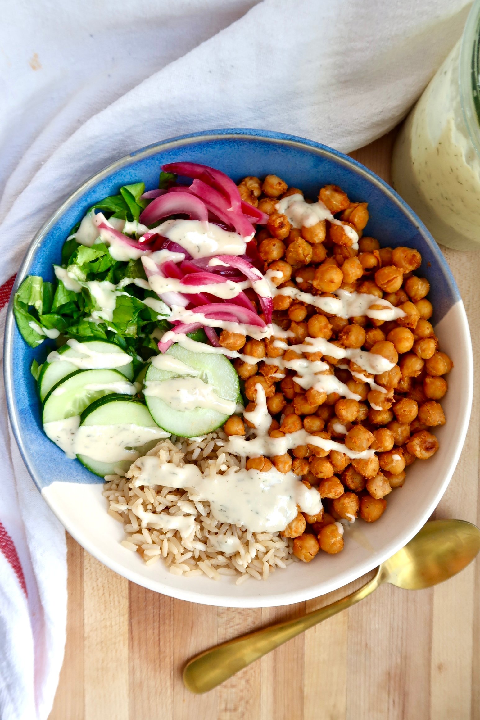 Grain bowl topped with buffalo chickpeas, cucumber, greens, pickled onions, and sauce.