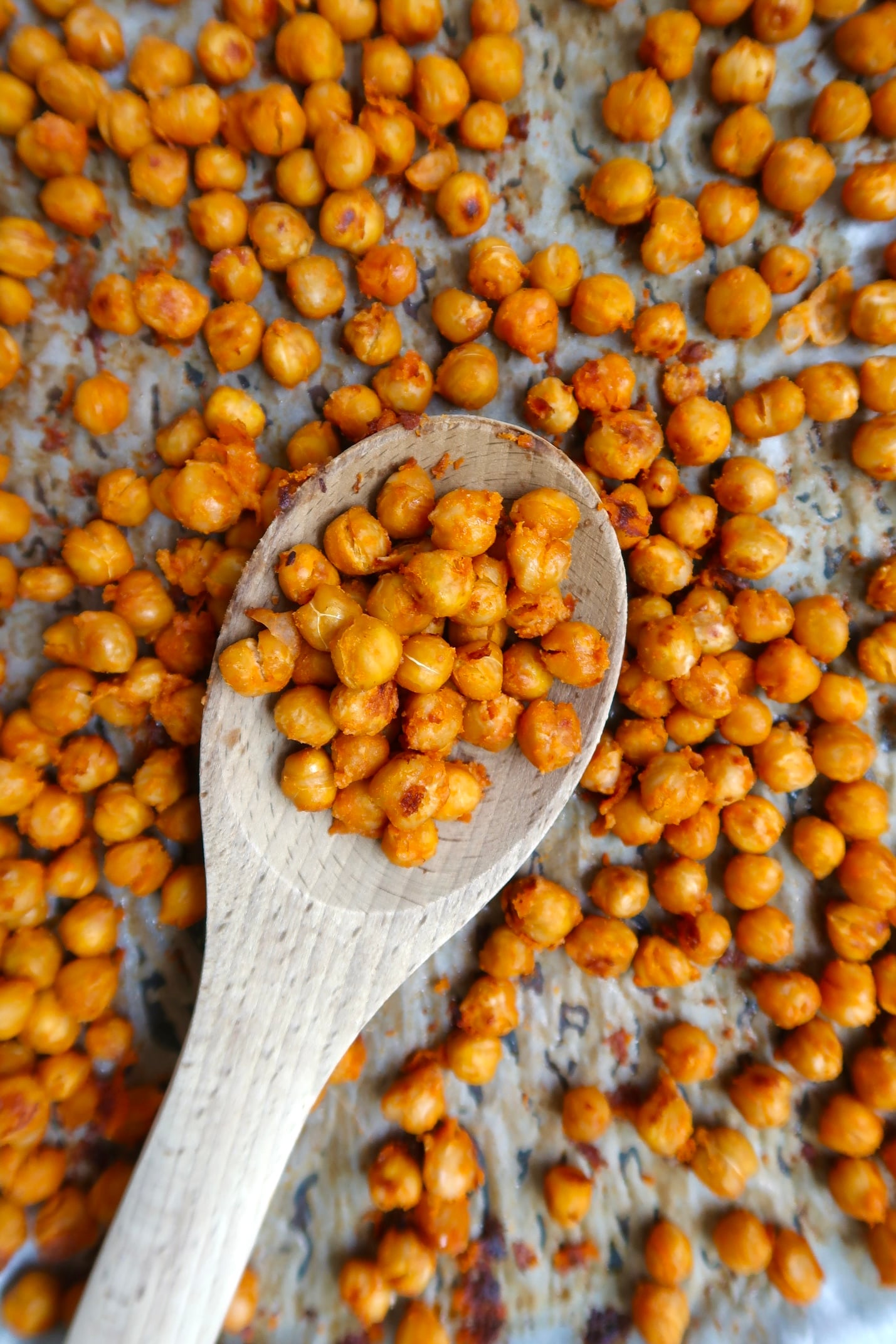Roasted chickpeas on a wooden spoon over a baking sheet.