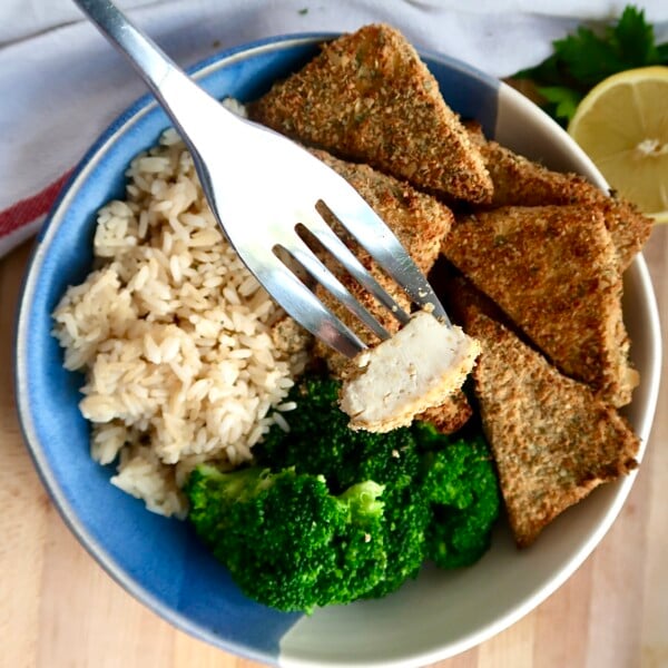 Bowl with breaded tofu, broccoli and rice and a fork piercing a piece of the tofu.