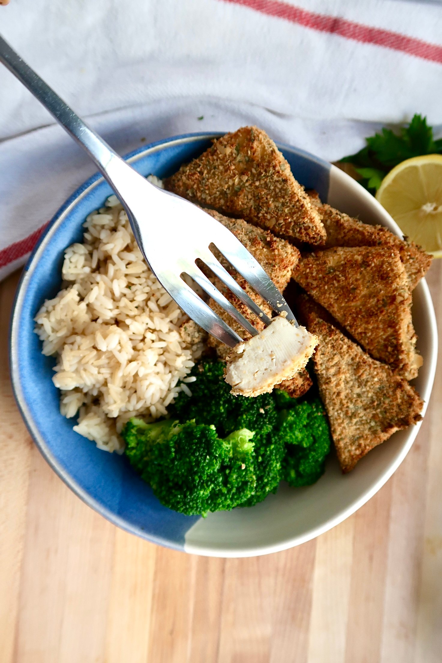 Bowl with breaded tofu, broccoli and rice and a fork piercing a piece of the tofu. 