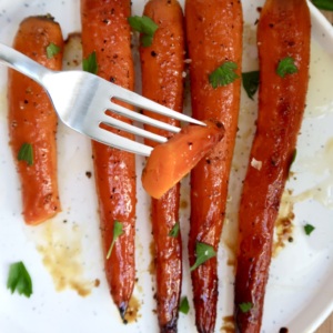 Fork with a piece of carrot on it and roasted carrots in the background.