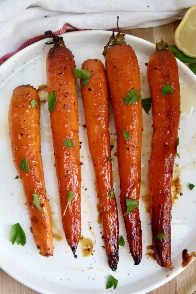 Whole roasted carrots on a plate with parsley on top.