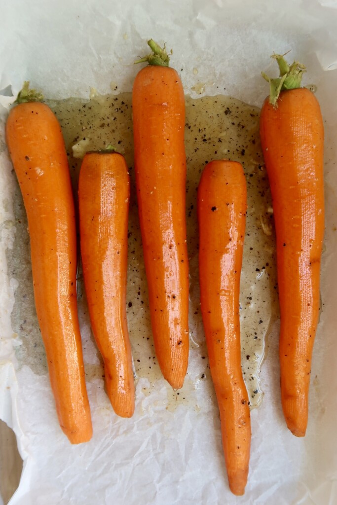 Uncooked carrots on a sheet pan with a glaze over top.