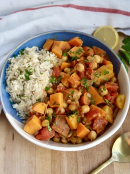 Side shot of bowl with curry, rice, and parsley on top with lemon on the side.