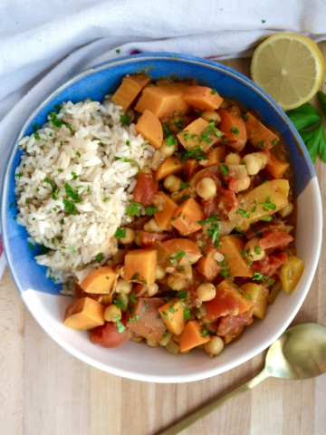 Bowl with curry, rice, and parsley on top with lemon on the side.