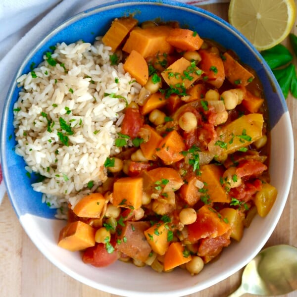 Bowl with curry, rice, and parsley on top with lemon on the side.