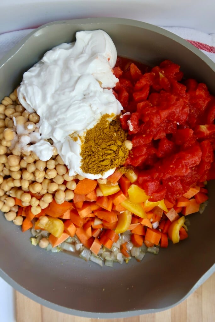 Chickpeas, coconut milk, carrots, peppers and tomatoes in a pot with spices.