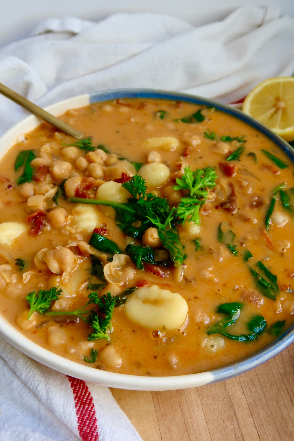 Side view of a bowl with creamy gnocchi soup with spinach, chickpeas and sundried tomatoes and a spoon scooping some.