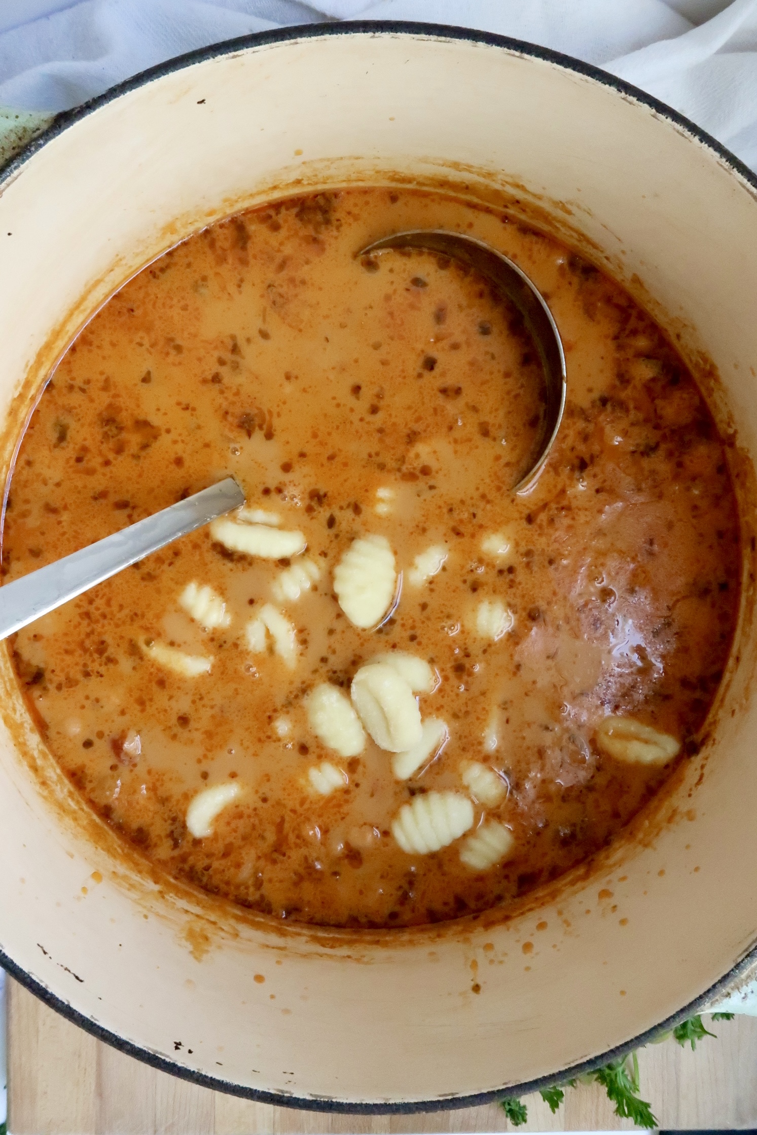 Pot with coconut milk with tomato paste and spices with gnocchi in the soup and a ladel scooping some.