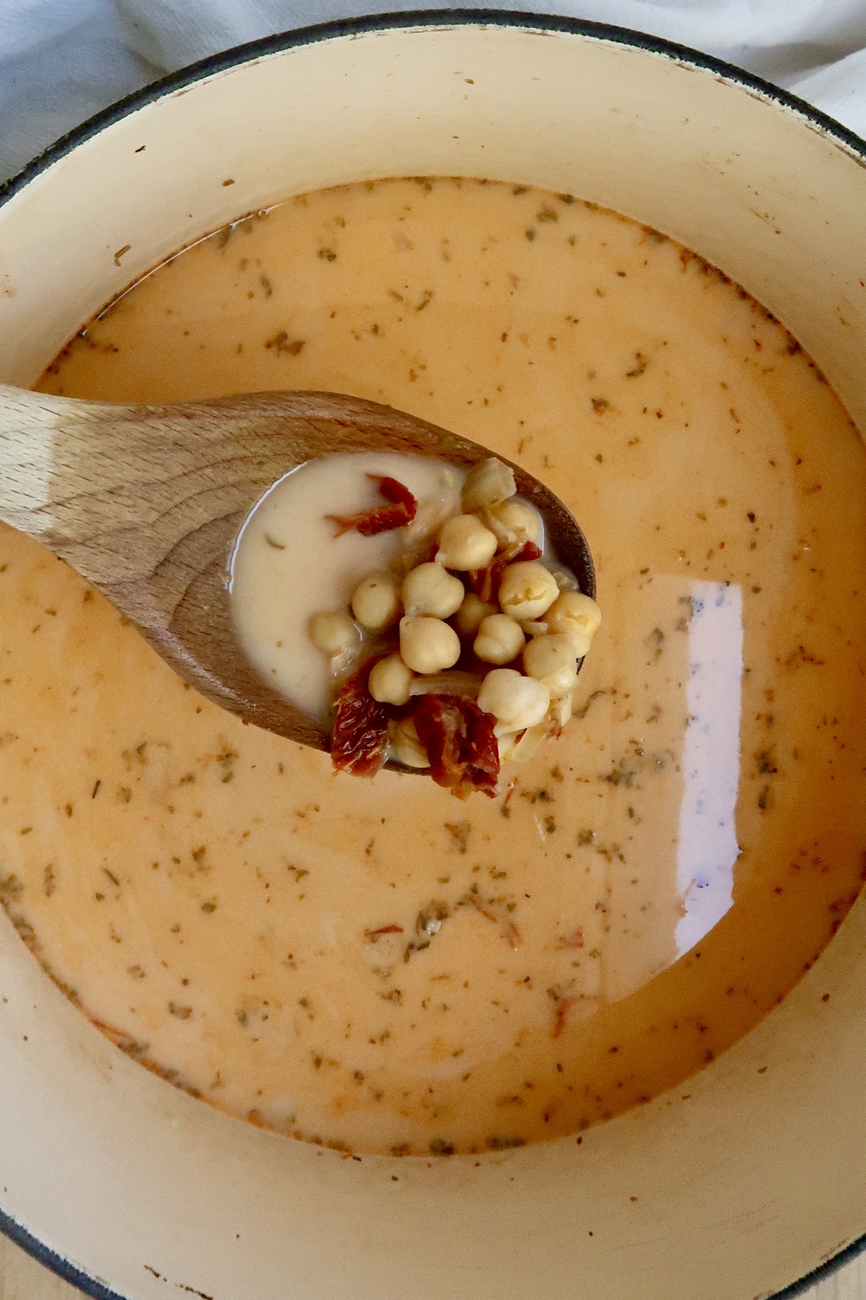 Pot with coconut milk, oregano, sundried tomatoes and chickpeas and a spoon scooping some.