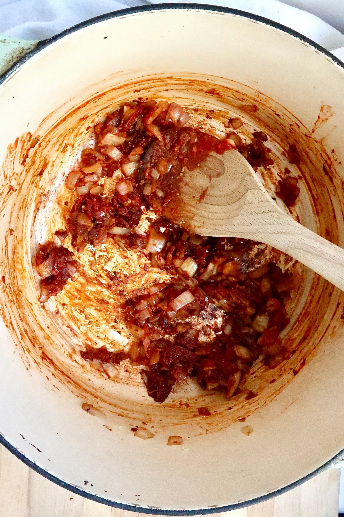 Pot with wooden spoon stirring yellow onion, tomato paste and sundried tomatoes.