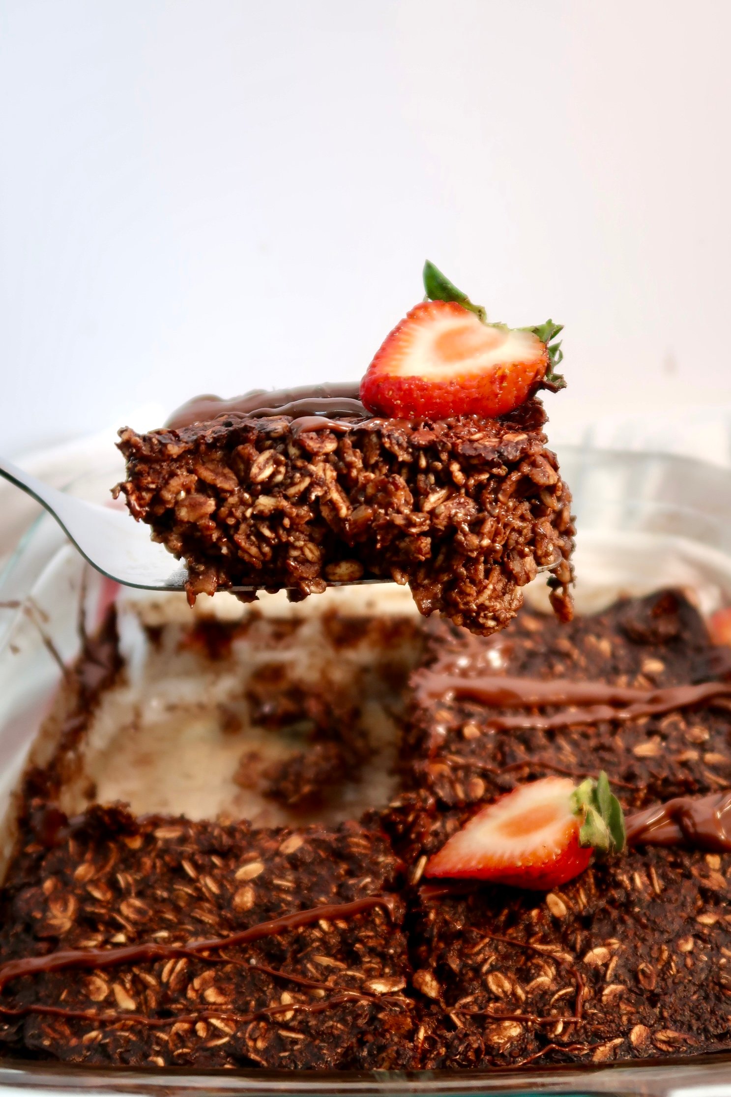 Pan of chocolate baked oats and a slice of chocolate oats being lifted by a spatula. 