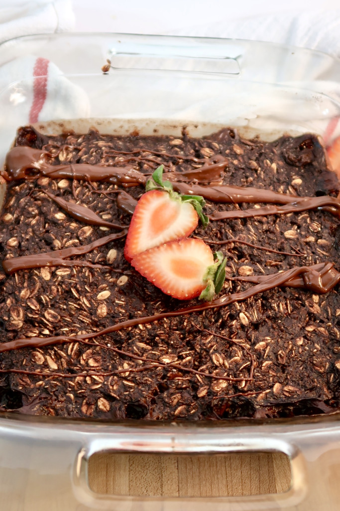 Baking dish with baked chocolate oats inside and a drizzle of melted chocolate on top and a sliced strawberry on top.