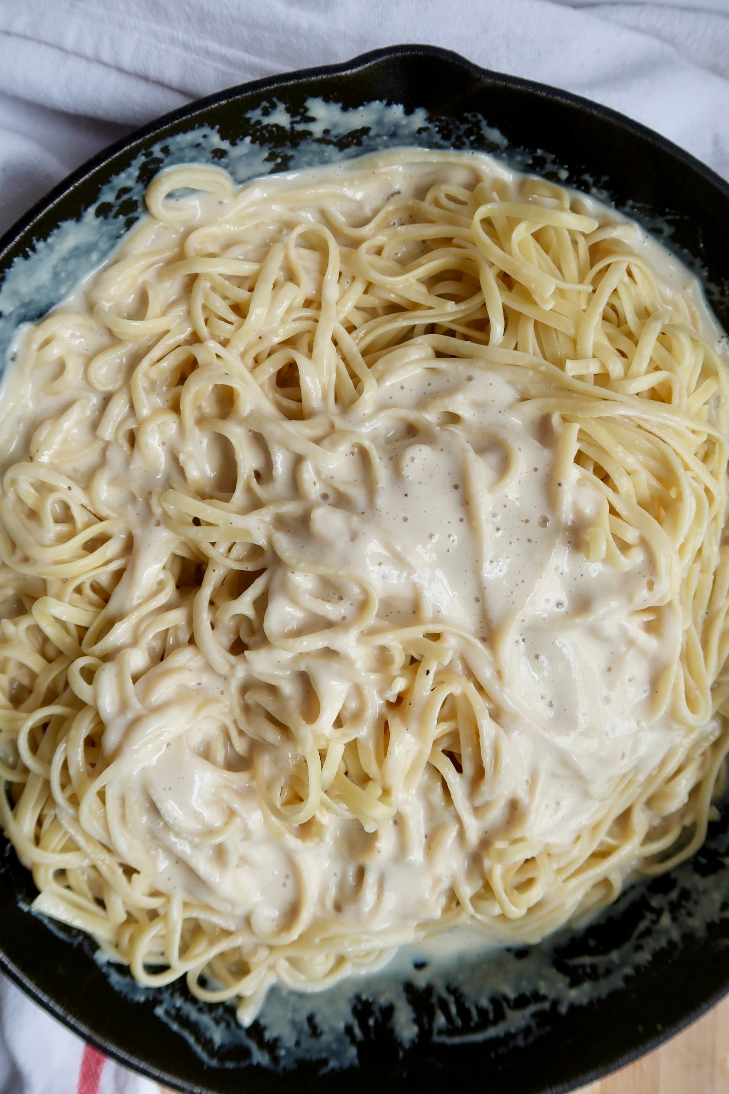 Cast iron pan with linguine being mixed with silken pasta sauce.