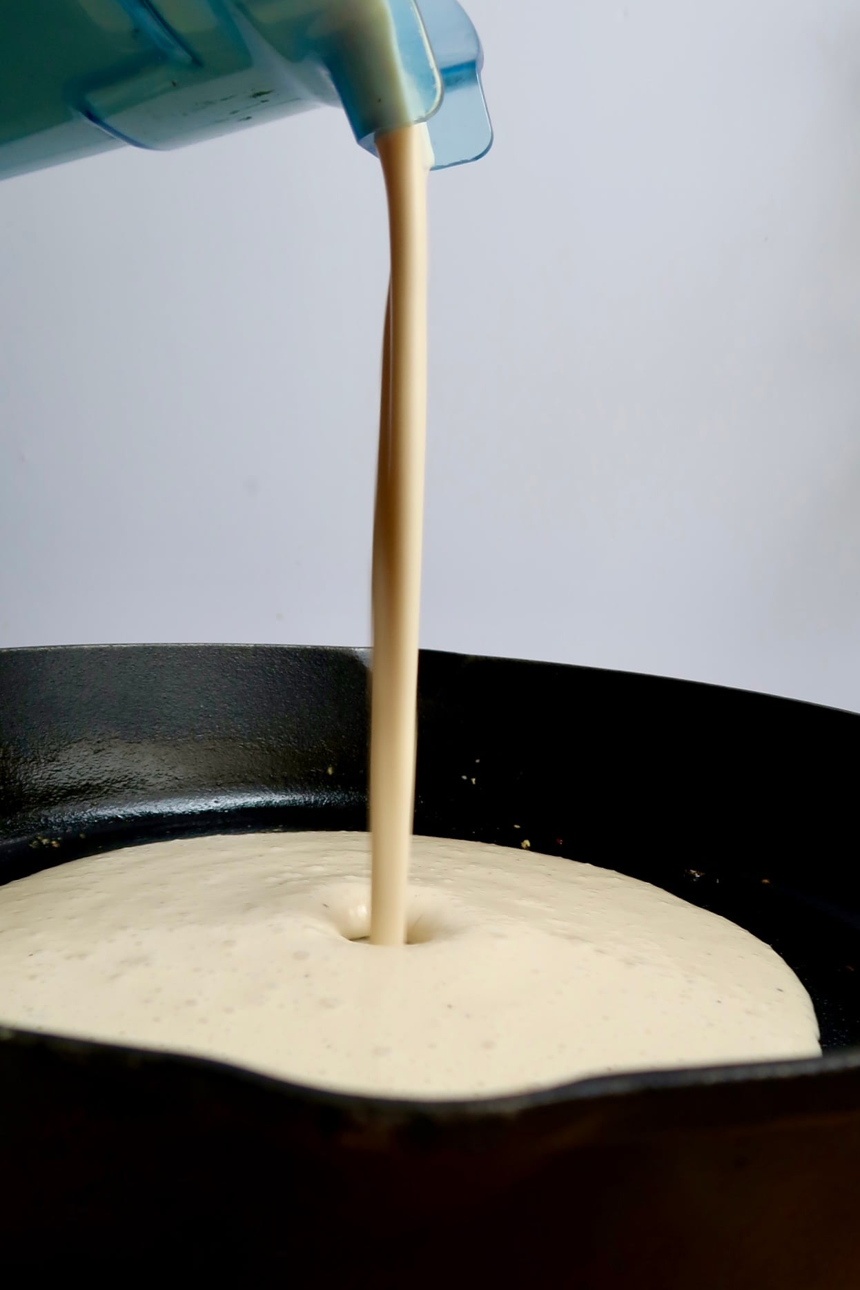 Pasta sauce being poured into a cast iron pan.