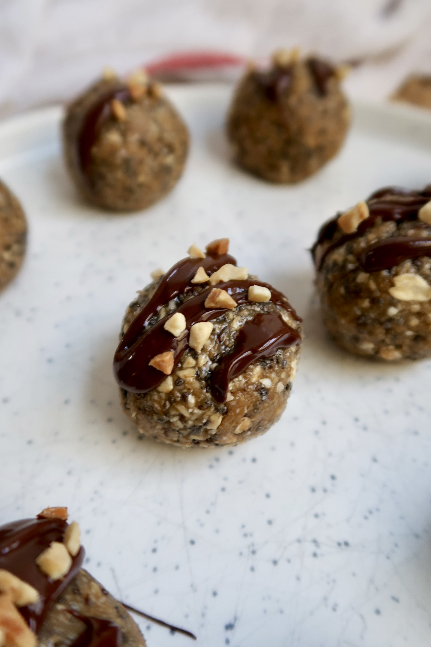 Close up of energy ball with oats, peanut butter and chia seeds with chocolate drizzled on top and peanut pieces.
