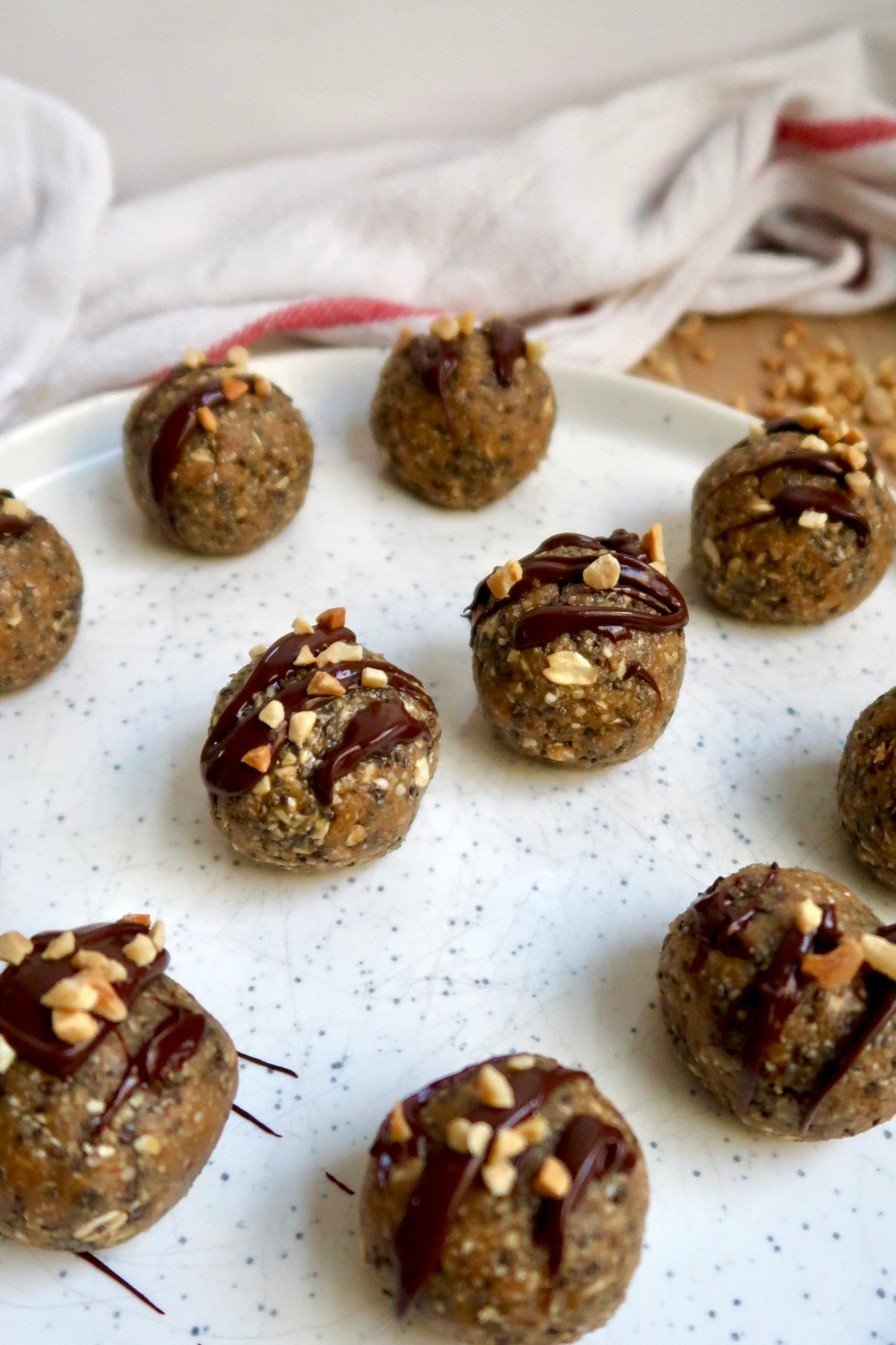 Side view of plate with energy balls drizzled with chocolate and peanut pieces on top.