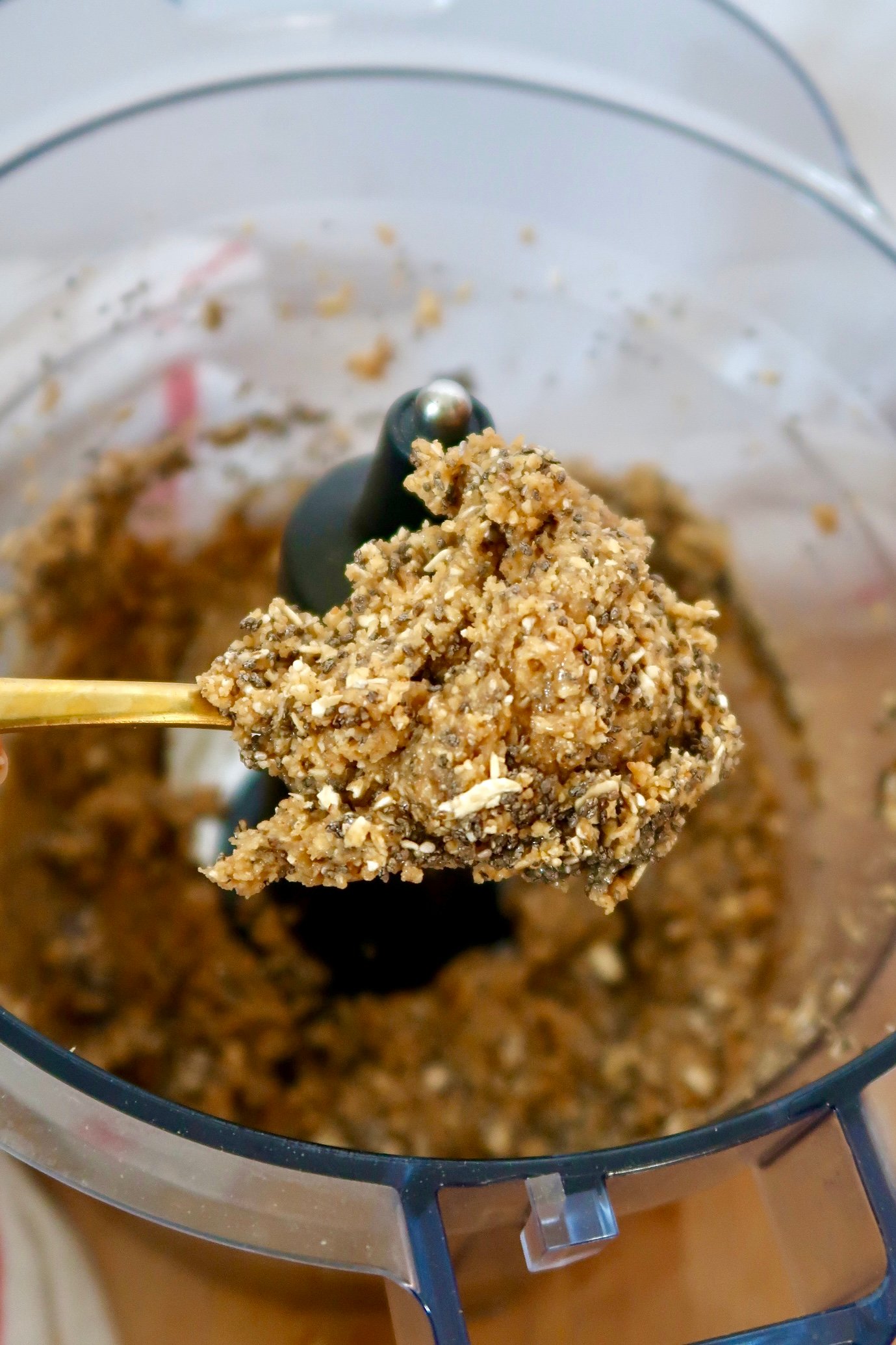 Spoon scooping peanut butter energy bite batter of peanut butter, oats, chia seeds and a food processor in the background.