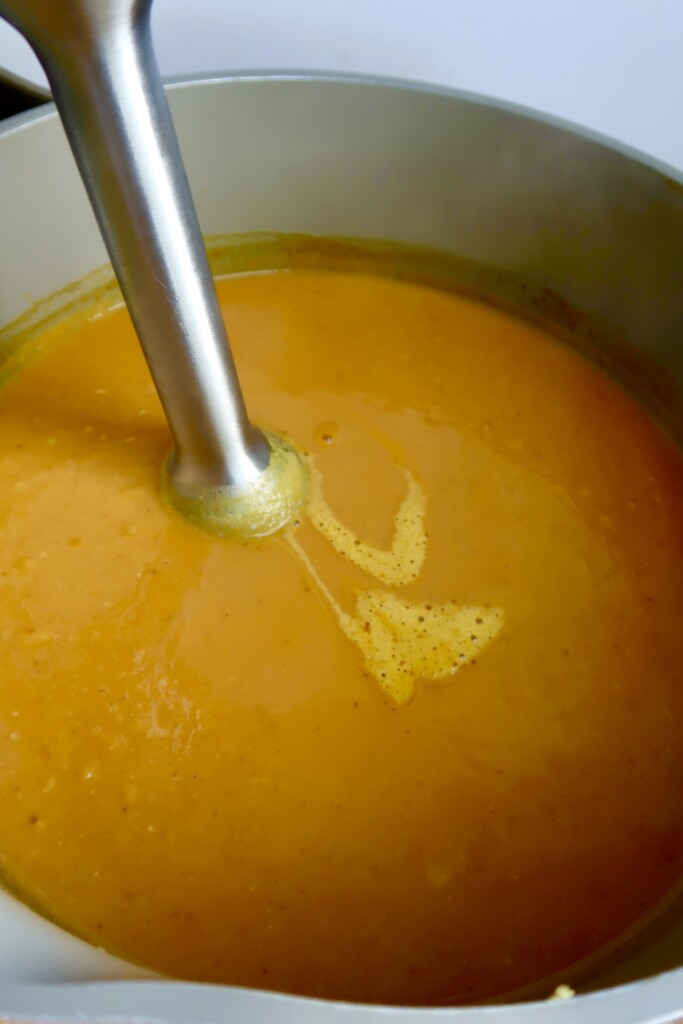 Pot with pumpkin soup and an immersion blender inside.