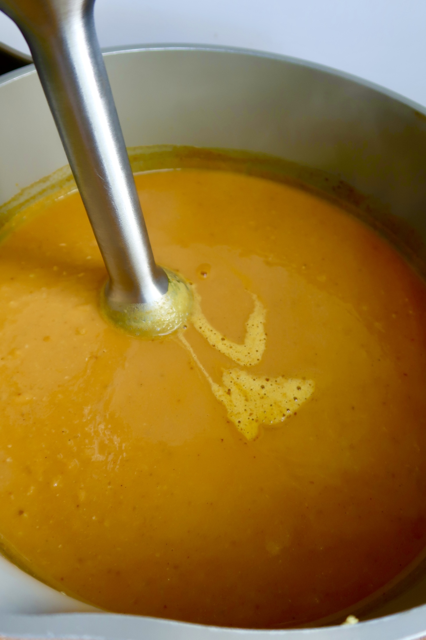 Pot with pumpkin soup and an immersion blender inside.