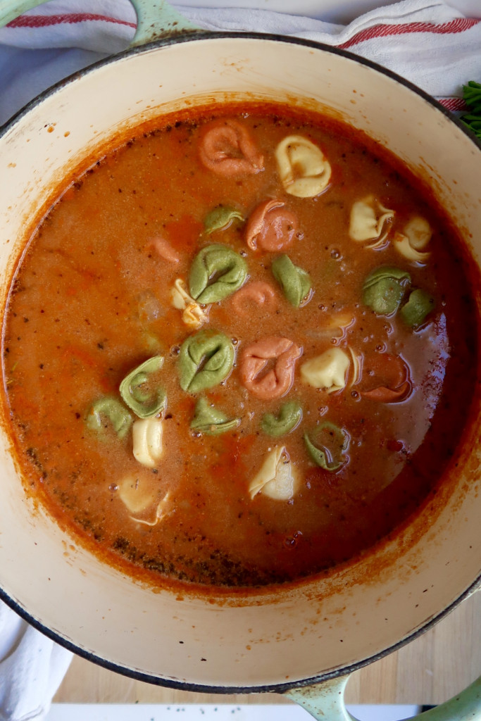 Large pot with tomato soup in it and tortellini.