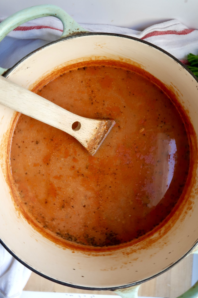 Large pot with tomato soup in it and a wooden spoon.