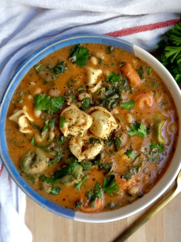 Blue and white bowl with soup with tortellini, kale, basil, and basil off to the side.