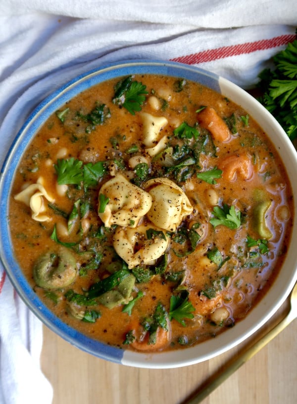 Blue and white bowl with soup with tortellini, kale, basil, and basil off to the side.