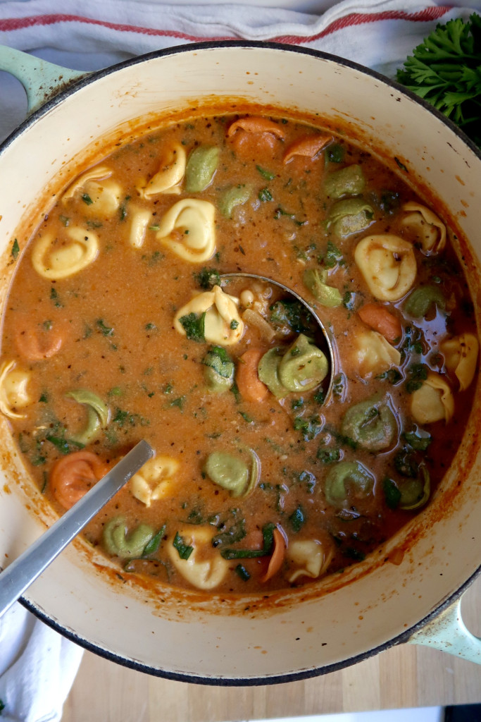 Large pot with tomato soup, wilted kale, and tortellini and a ladel scooping some.