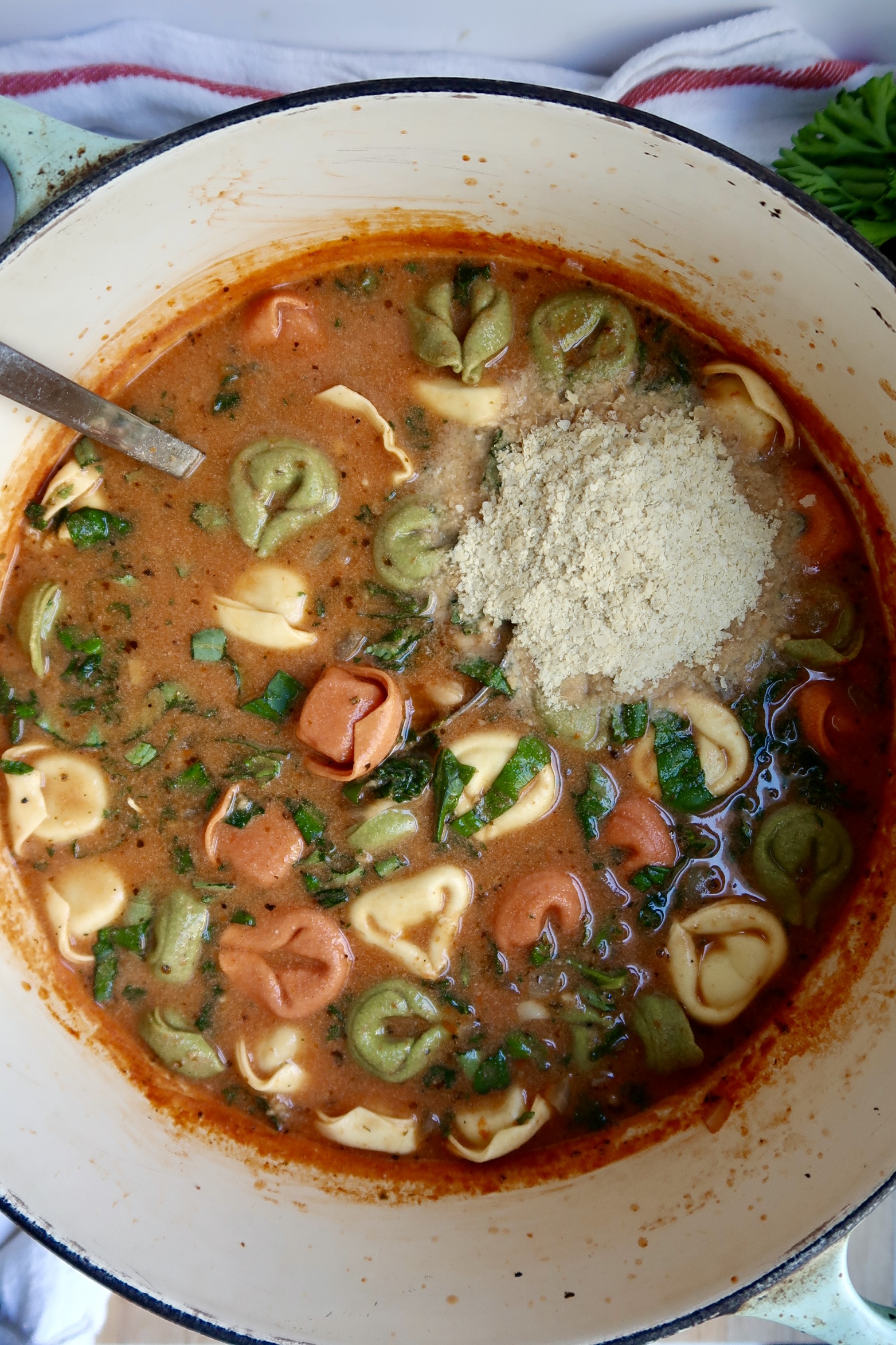 Large pot with tortellini with basil wilted in and nutritional yeast on top.