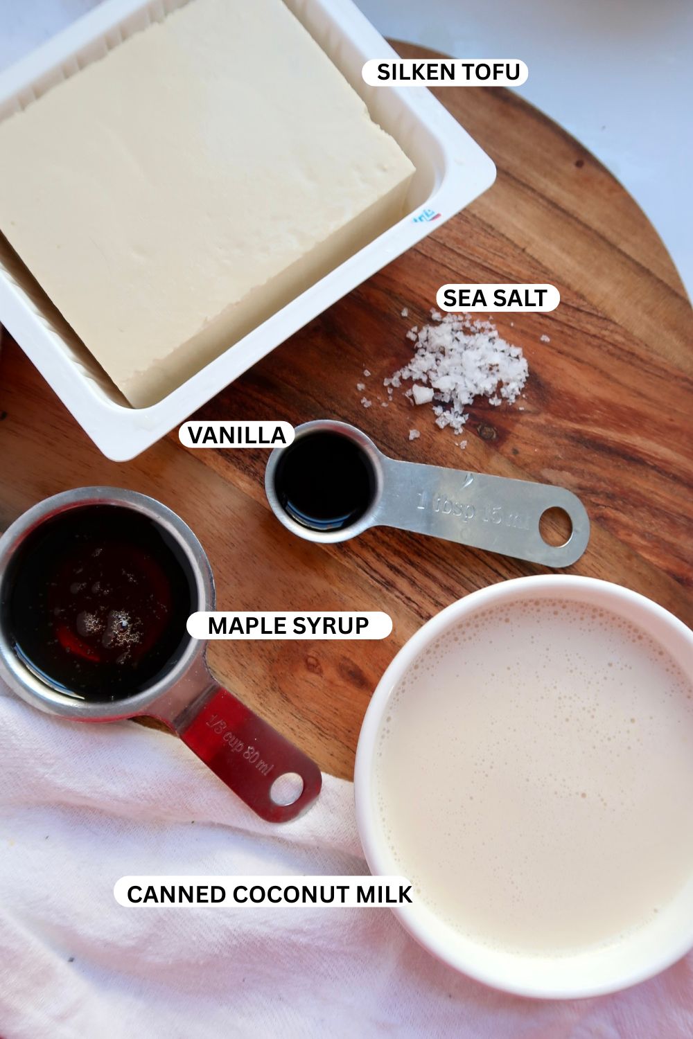 Silken tofu, coconut milk, maple syrup, vanilla extract and salt on a cutting board.