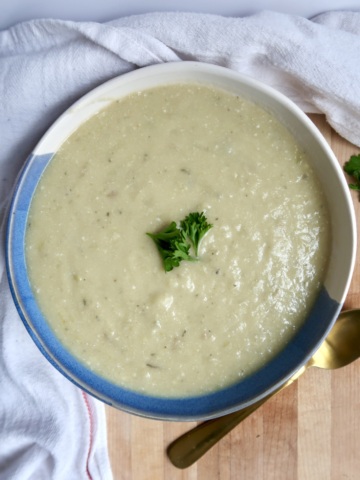 Potato leek soup in a bowl with a gold spoon to the side and parsley as garnish.