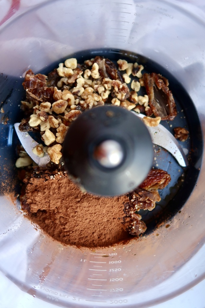 Food processor with dates, walnuts, cocoa powder inside.