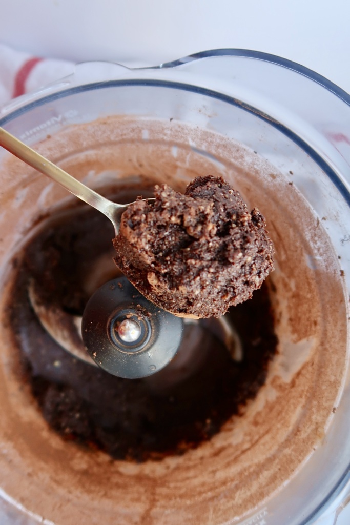 Blended energy ball dough in a food processor with a spoon scooping some.
