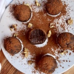 A plate of brownie energy balls with one half bitten and cocoa powder sprinkled on top.