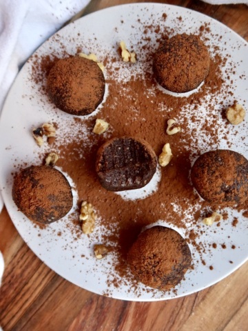 A plate of brownie energy balls with one half bitten and cocoa powder sprinkled on top.